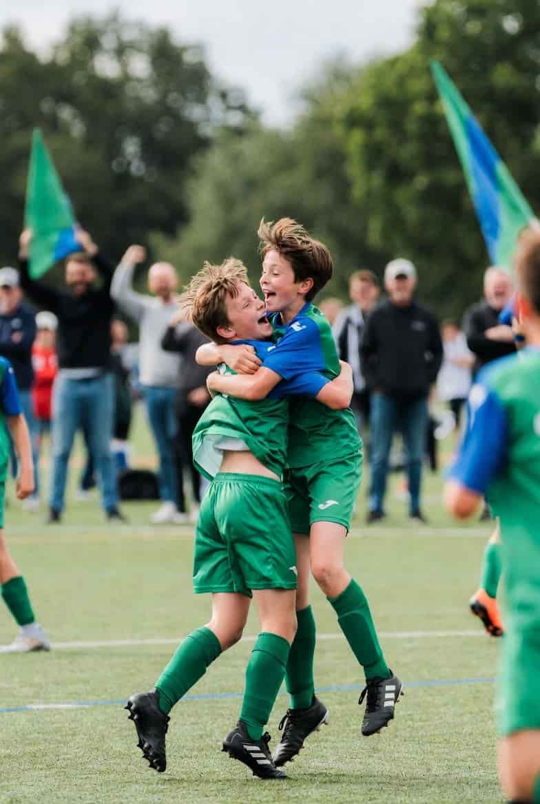 Two teammates leaping into each other after a goal, flags up behind them