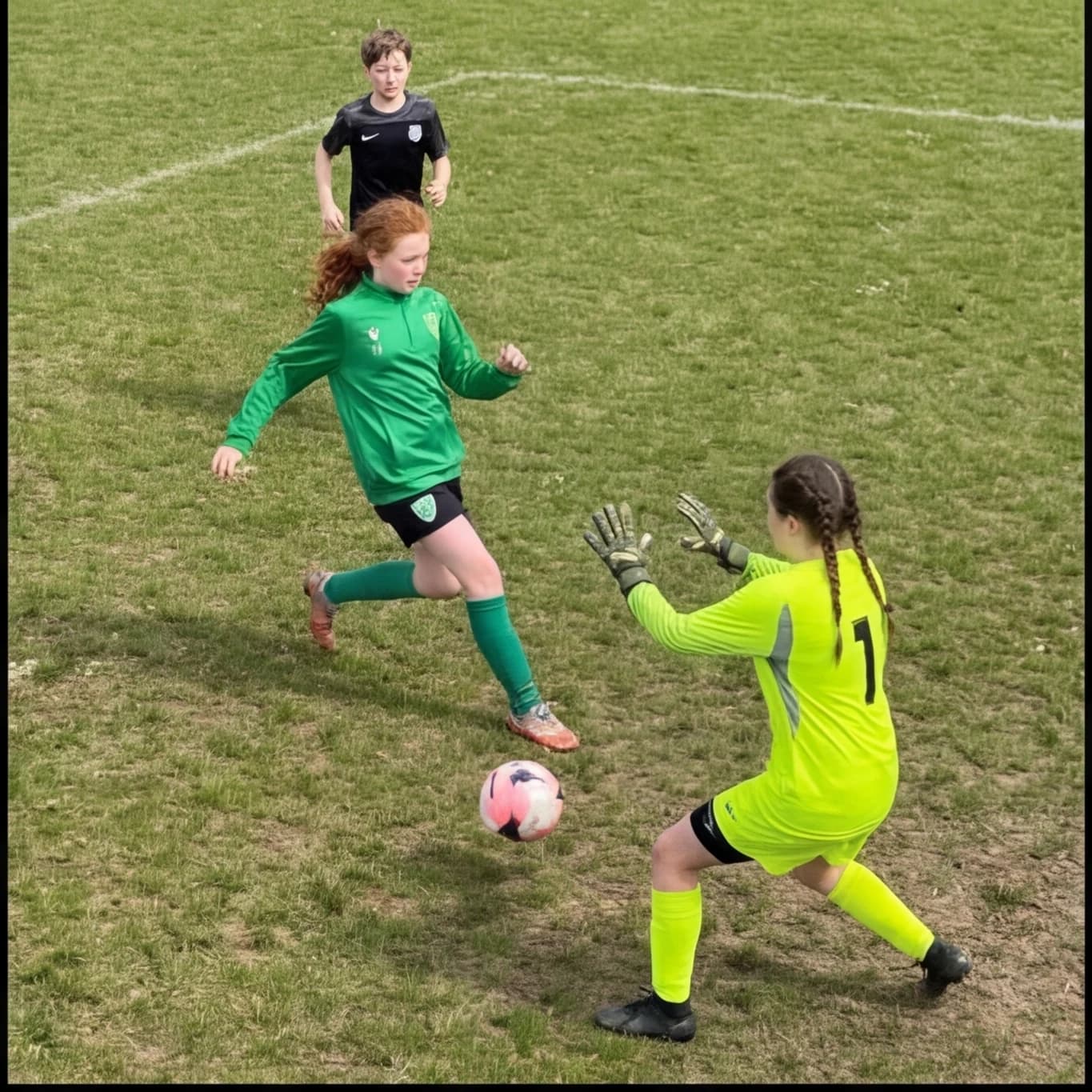 A girl in green closing down a goalkeeper one on one, a teammate arriving in support