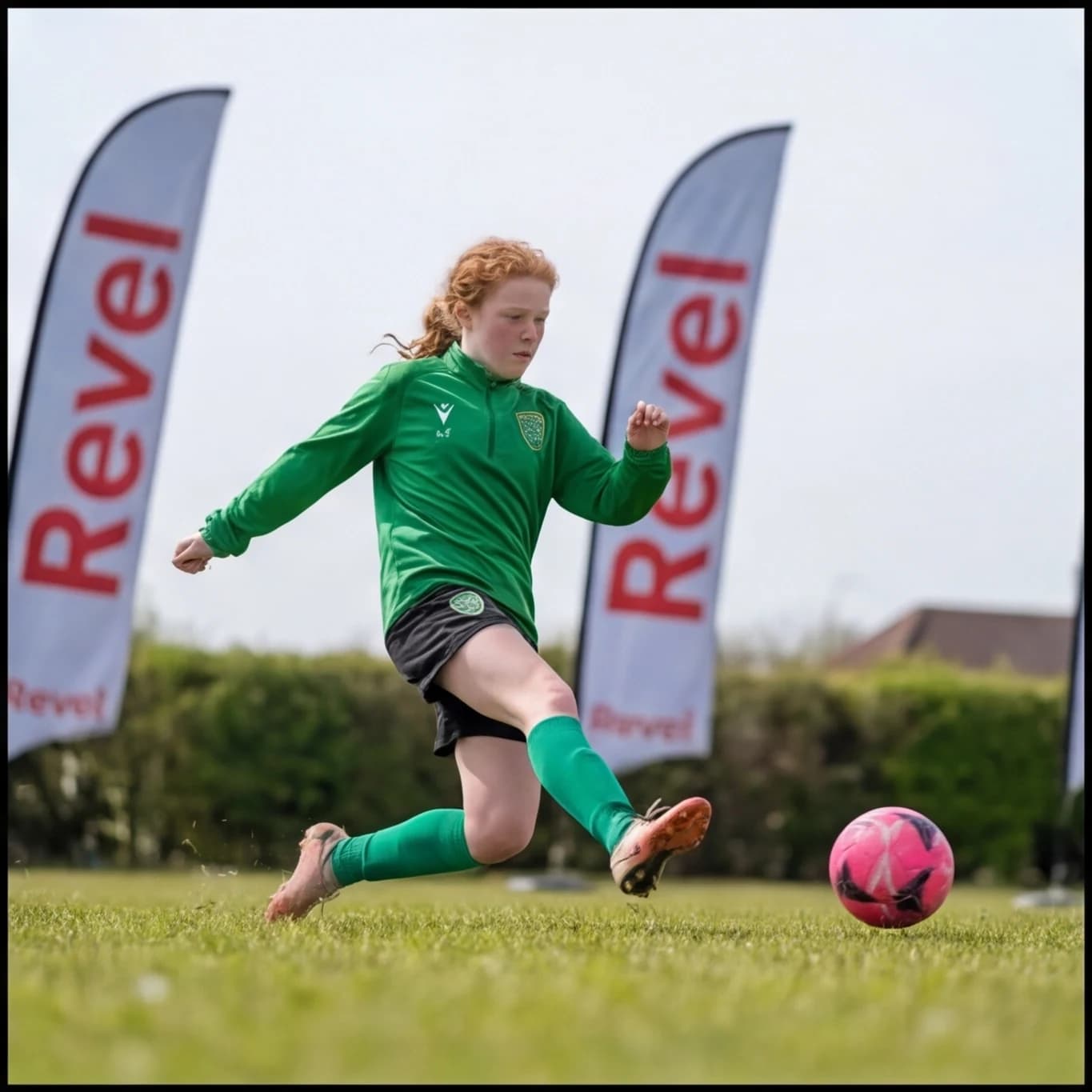 A girl in green striking the ball low, Revel flags either side of her